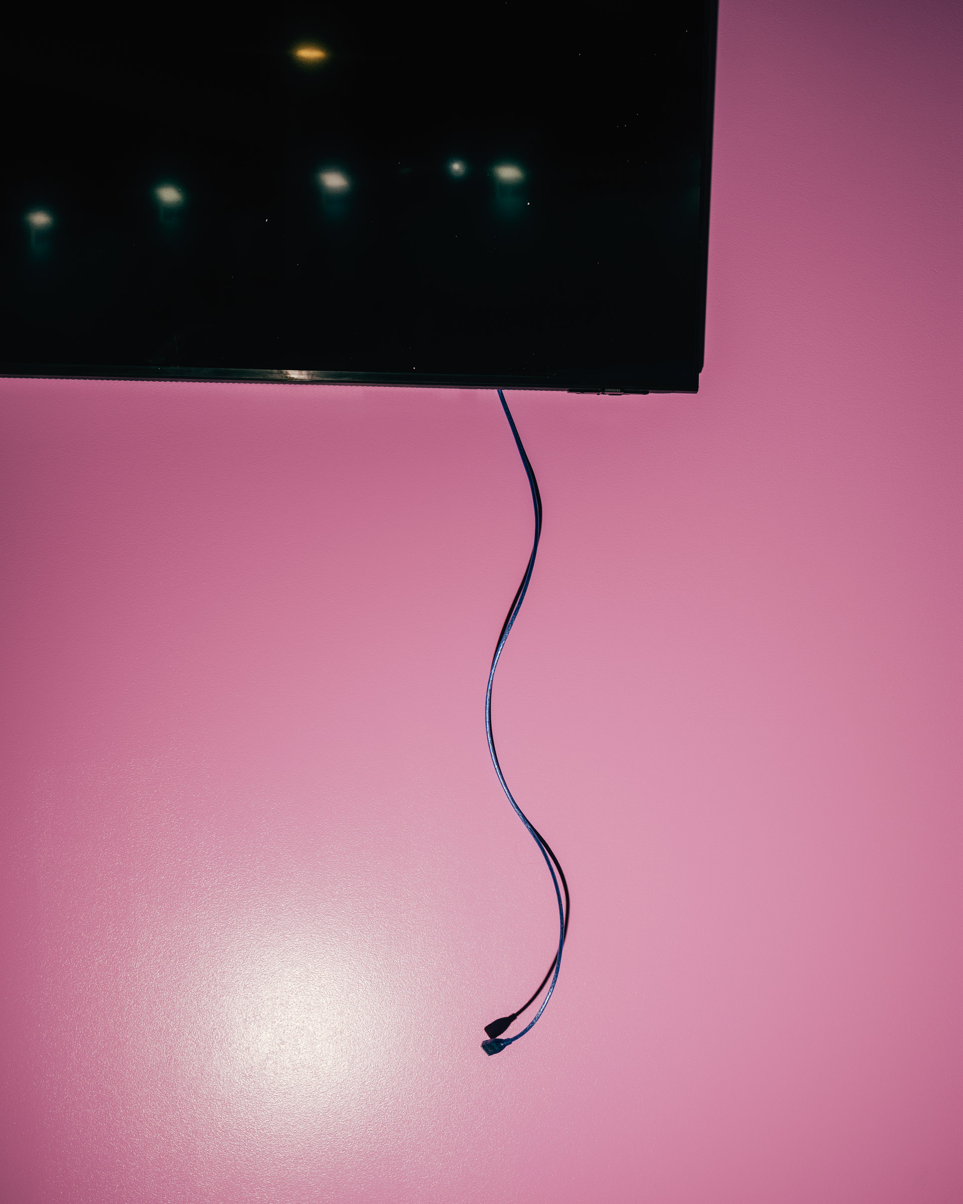 Schwarzer Bildschirm mit Kabel auf rosa Wand. 