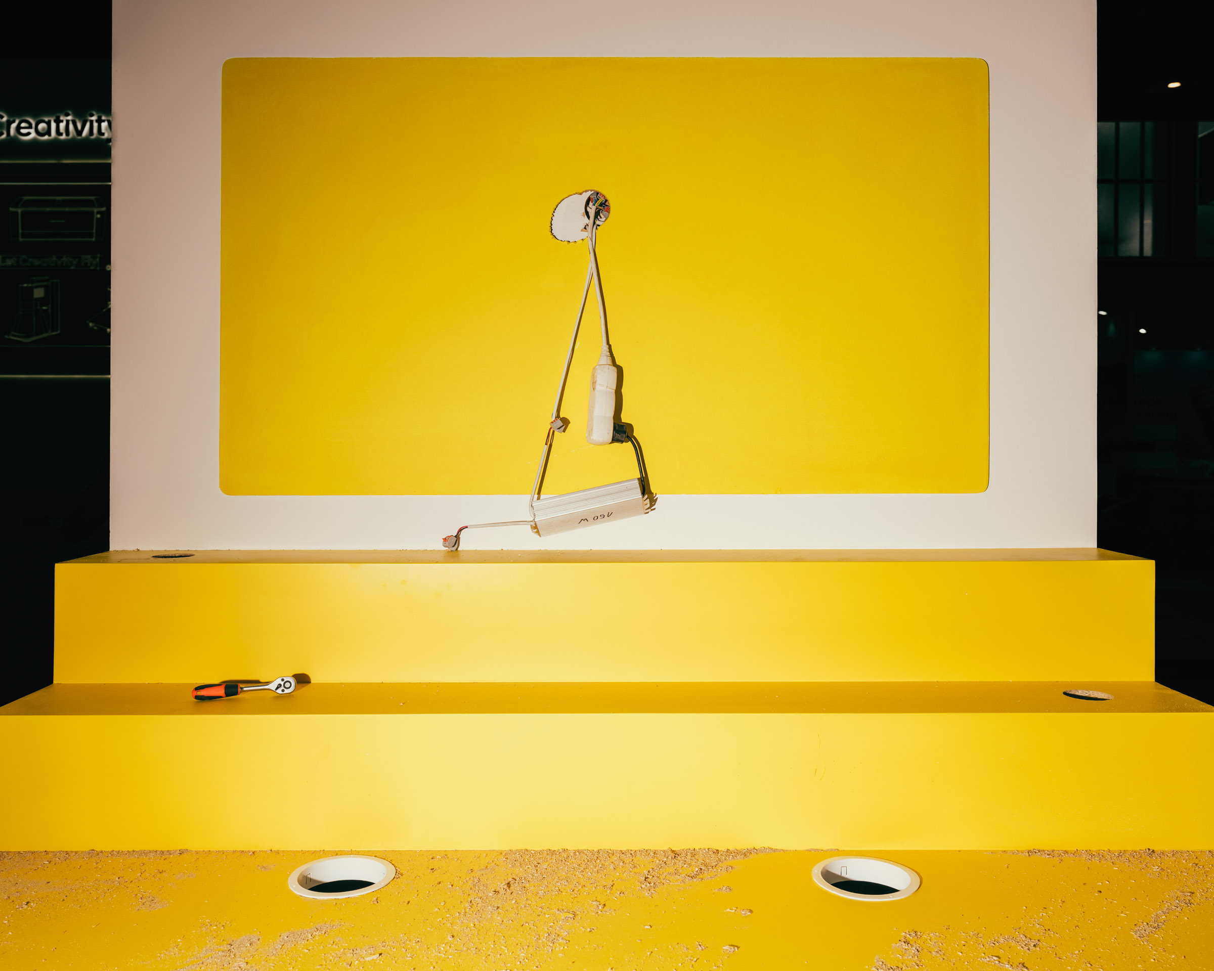 Werkzeug und Kabel auf gelbem Podest vor gelber Wand. 