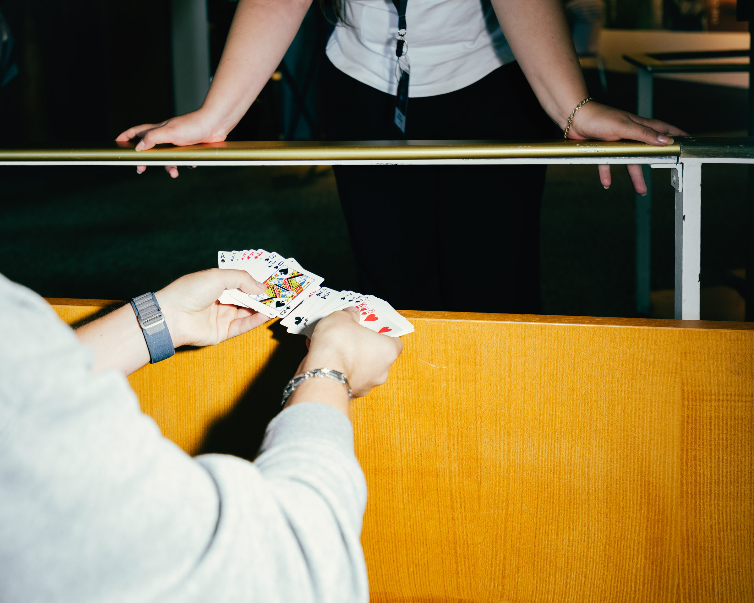 Hände halten Spielkarten über Holztresen. 