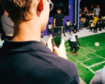 Mann filmt Roboter-Fußballspiel mit seinem Smartphone.