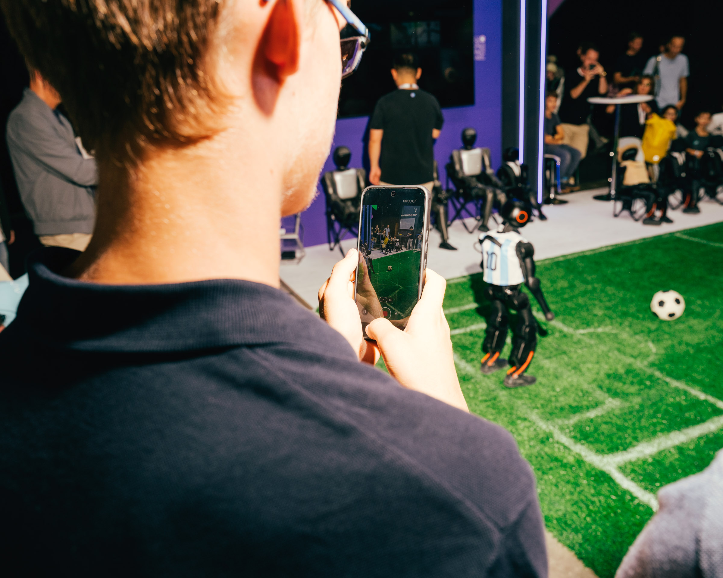 Mann filmt Roboter-Fußballspiel mit seinem Smartphone. 