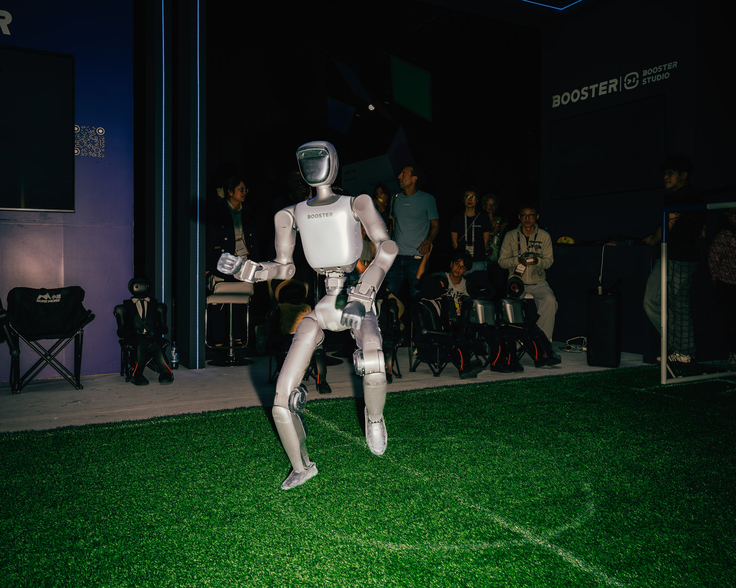 Roboter auf Kunstrasen mit Zuschauern im Hintergrund. 
