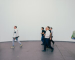 Menschen gehen in einer Galerie an einer weißen Wand entlang.