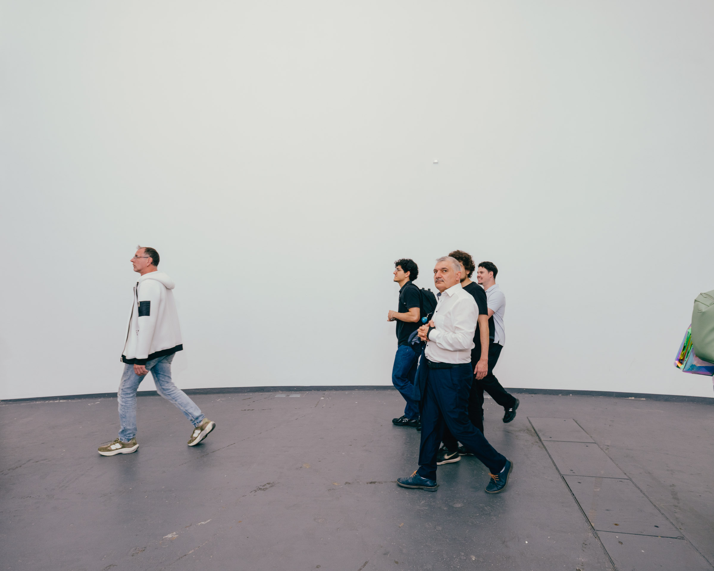 Menschen gehen in einer Galerie an einer weißen Wand entlang. 