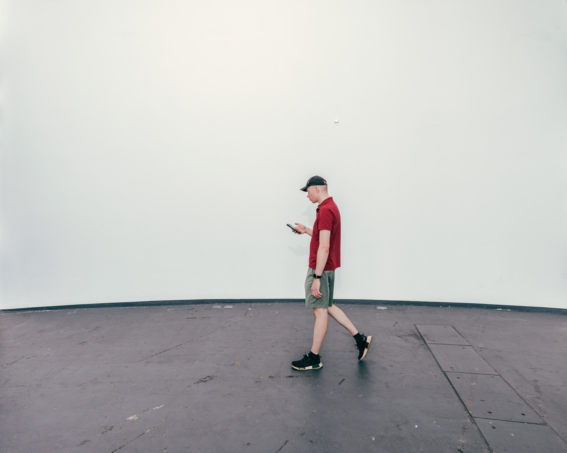 Mann mit Smartphone geht vor weißer Wand. 