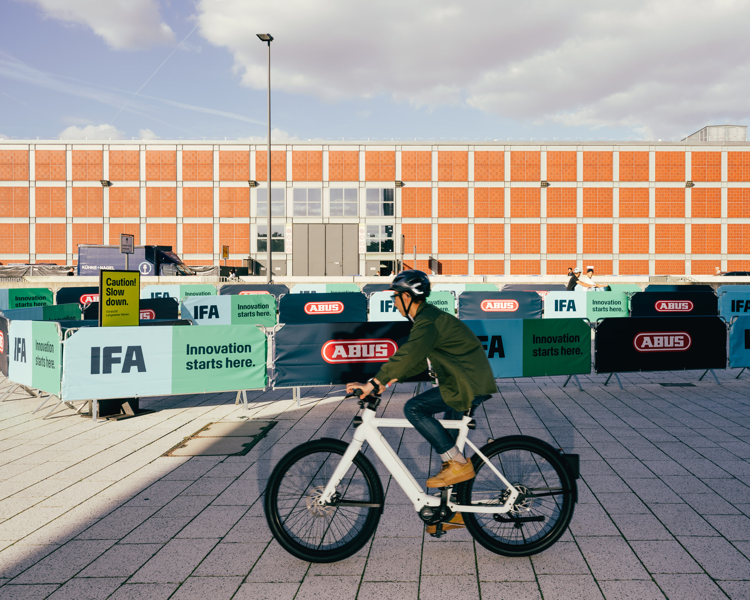Fahrradfahrer vor IFA-Bannern und Backsteingebäude. 