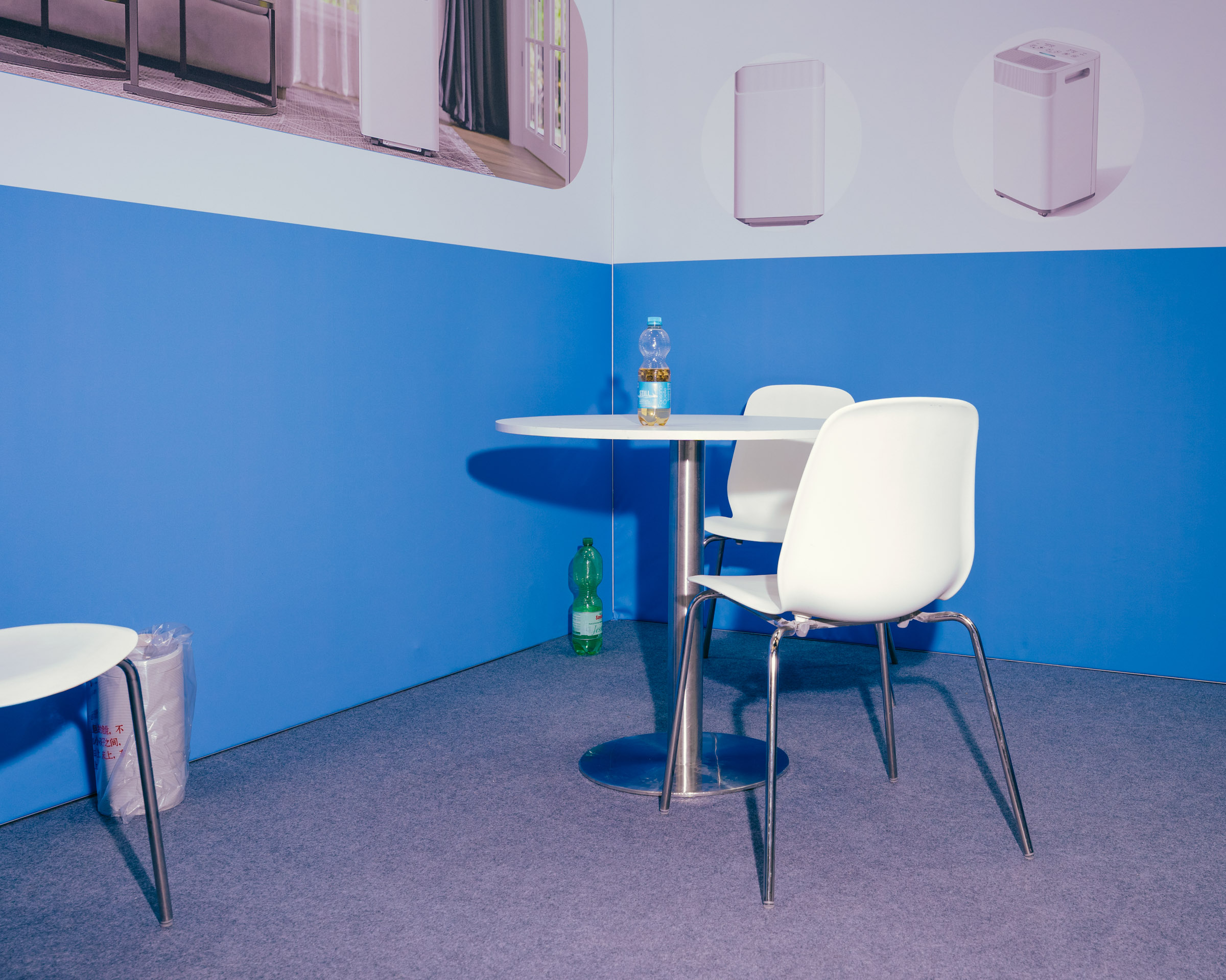 Weiße Stühle und Tisch mit Wasserflaschen auf blauem Hintergrund. 