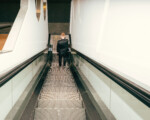 Mann im Anzug fährt Rolltreppe hinunter.